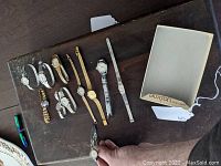 Overhead view of 10 assorted women's wristwatches with various metal bands and a Buxton watch box on a dark surface.