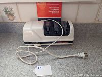 Electric countertop knife sharpener unit with power cord coiled in front.