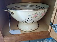 Front view of cream enamel colander with floral decoration, gold rim and pedestal base