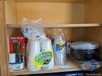 Shelf with various food storage and serving items including plastic cups, grill foil pack, and green glass cruet box