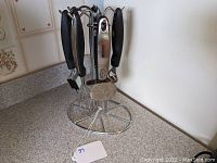 Full view of stainless steel rotating kitchen tool stand with five hanging tools showing handles and part of the stand.