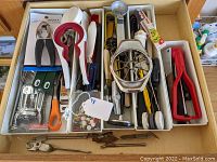 Wide view of the kitchen tool drawer showing assortment of items including food mill, peelers, tongs, scoops