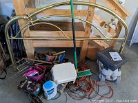 Wide view showing brass headboard, floor jack, push broom, various hand tools in toolbox, and extension cords.