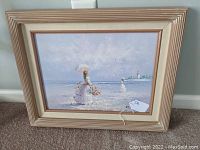 Framed oil painting showing a Victorian lady with parasol and basket at a beach setting with a shoreline and lighthouse in the background.
