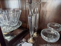 Pair of tall glass bud vases with sterling silver bases on wooden shelf, one vase with fluted top edge and floral etching