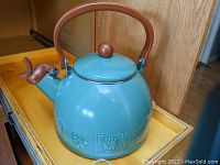 Side view of green ceramic tea kettle with decorative nature pattern, showing wooden handle and spout cover.