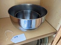 Three stainless steel mixing bowls nested inside each other on a wooden shelf, one large plain bowl visible