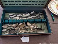 Photo of mixed silverware including stainless steel utensils and tarnished coin silver pieces arranged inside a lined case.
