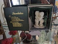 Photo of Snowbabies figurine in original box with visible black and white speckled box interior and figurine inside.