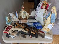 Overview photo of religious statues, crucifixes, rosaries and figurines arranged on a table.
