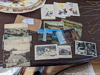 Photo showing several vintage postcards and greeting cards laid on a table including black and white postcards depicting houses, city, and seagulls along with colored landscape postcards and greeting cards with illustrations.