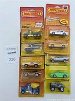 Group photo of 10 Matchbox cars and vehicles sealed in blister packs arranged vertically in two columns; varied colors and models visible; includes cement trucks, cars, helicopter and SUV.