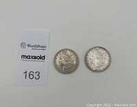 Two 1882 US Morgan Silver Dollars photographed front side (obverse) with sale tag nearby.