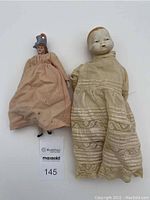 Two antique porcelain dolls, one in a pink dress and one in a cream dress, laid side by side showing general condition