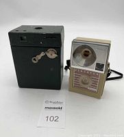 Photo showing both vintage cameras side by side, green Kodak box camera and Kodak Flashfun Hawk-eye No.2 Model B with large flash reflector and neck strap.