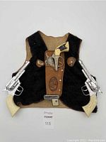 Front view of the black faux fur cowboy vest with toy cap guns and brown toy holster attached. Two toy cap guns with silver barrels and cream handles are attached to the sides and one brown and silver toy gun in the holster in the center.