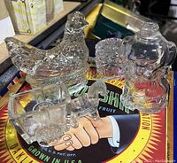 View of four glass candy containers shaped as a hen, donkey with cart, dog, and figure with top hat arranged on a table.