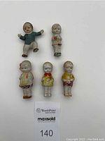 Top view of all five miniature Japanese bisque dolls showing their painted clothes and condition.