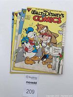 Five Walt Disney comic books stacked showing front covers with characters including Donald Duck and Daisy Duck.