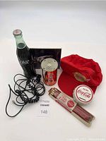 Lot overview including Coca-Cola glass bottle, red transistor radio styled as Coke can, piggy bank, pencils, telephone cords, and red cap.