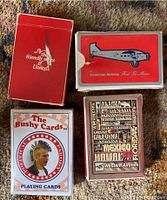 Eight decks of airline playing cards shown in a red case inside. Decks include United Airlines, American Airlines, Western Airlines, Bushy parody cards, Northwest, and Pan Am. Some card boxes are open and others are closed.
