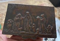Bronze top lid with embossed detailed figurative scene featuring classical or Renaissance-style people and cherubs in relief.