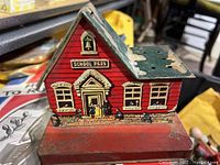 Front view of the antique German tin litho school house with red walls, front door, windows, bell tower, and base.