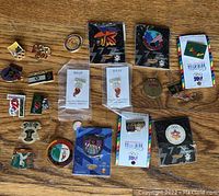Top-down view of all Olympic pins spread out on a wood floor showing diversity of pins and some original packaging