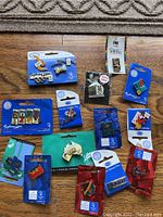 Photo showing multiple Sydney 2000 Olympics enamel pins on original cards, colorful with some mascot and event logos, arranged on floor.