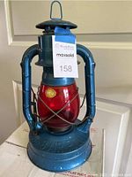 Full view of blue metal Dietz kerosene lantern with red glass globe and carrying handle on top.
