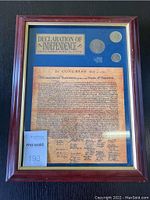 Full view of framed Declaration of Independence with coins and label mounted on blue mat in wood frame.