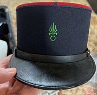 Front view of the kepi showing the green insignia and black visor.