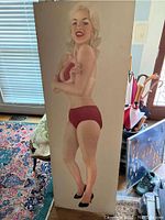 Front view of full life size print of Jayne Mansfield wearing red bikini, mounted on board, showing scratches and wear