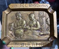 Front view of brass ashtray depicting WWII peace talks with German soldiers seated around a table; inscriptions include '7-5 REIMS 1945' and 'CAPITULATION'