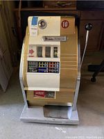 Full front view of cream and gold cabinet, lever, coin slot and payout window filled with dimes.