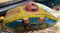 Side view of the yellow, blue, and red tin toy tank bank showing the graphics and coin slot on the turret.