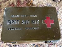 Top view of the green metal first aid kit box with red cross and text markings on lid.