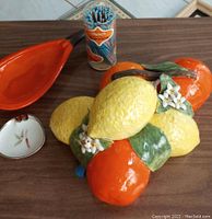 Overview photo showing ceramic fruit cluster, orange ceramic dish, floral ashtray, and package of paper straws on wooden table