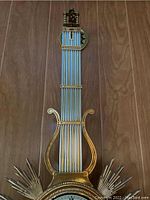 Front view of guitar-shaped wall clock showing gold and light blue neck design and top clock face with decorative elements.