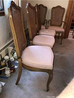 Four wood dining chairs with cane backs and pink upholstered seats lined against a wall.