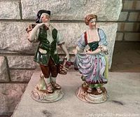 Front full view of porcelain man and woman figurines against stone background