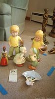 Photo showing six ceramic and metal figurines including two children, two ducks, and two metal statuettes in dresses.