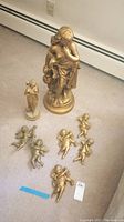 Overview of 8 gold-toned figurines including 6 cherubic angels and 2 larger classical-style statues
