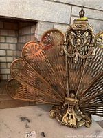 Front view of detailed fan-shaped metal fireplace screen next to a stone fireplace