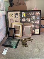 Multiple photo frames of various sizes including two multi-image collage frames, several small single photo frames, and two brass easels shown on carpet floor.