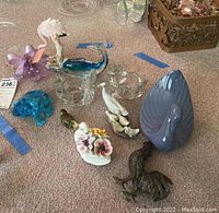 Overview of all animal figurines on carpet including glass flamingo, frog, dolphin, swan, ceramic swan, and floral piece plus blue ceramic bird and white bird with chicks.