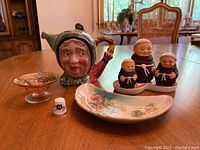 Photo showing Goebel monk salt and pepper shakers, Beswick teapot jam jar with lid and plastic demi spoon on plate, floral trinket dish, footed bowl with chip, and a thimble for scale.
