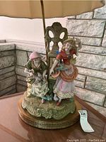 Close-up of vintage ceramic figurines forming the base of the lamp, showing detailed painting and minor chipping.