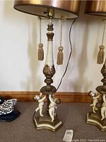 Front view of two vintage table lamps with cherub figurines at base, gold and cream tones, tassel-pull lampshades.
