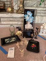 Overall lot arranged on floor and displayed near a fireplace hearth. Items include music box with blue flower in case, lacquer trays, glass cherub and butterfly ornaments, metal pitchers, a brass pot with ladle, and other decorative pieces.